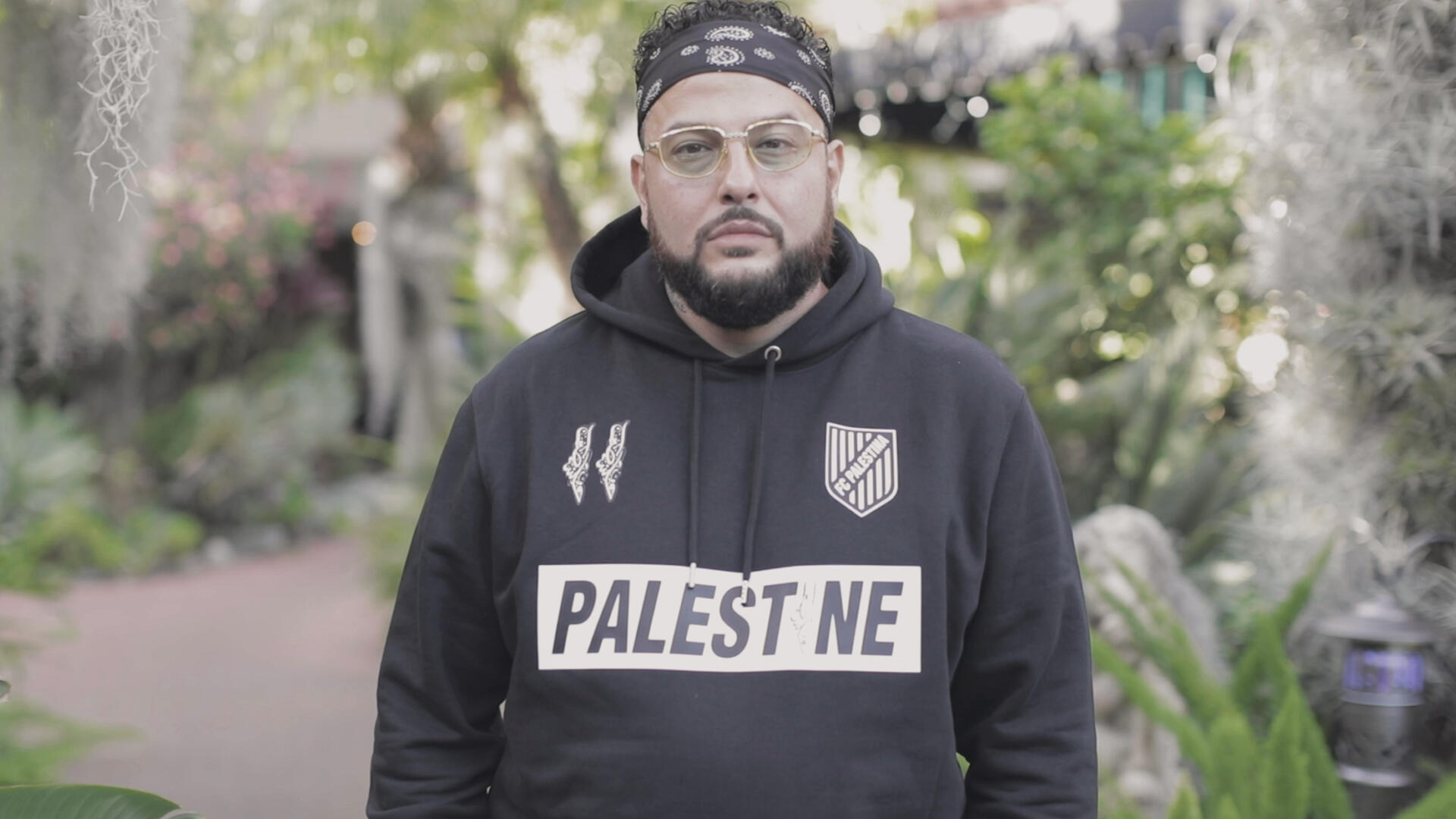 Rapper, songwriter and record producer Belly stands outside wearing a headband and sweatshirt with the text "Palestine" for a World Refugee Day 2021 photo shoot.