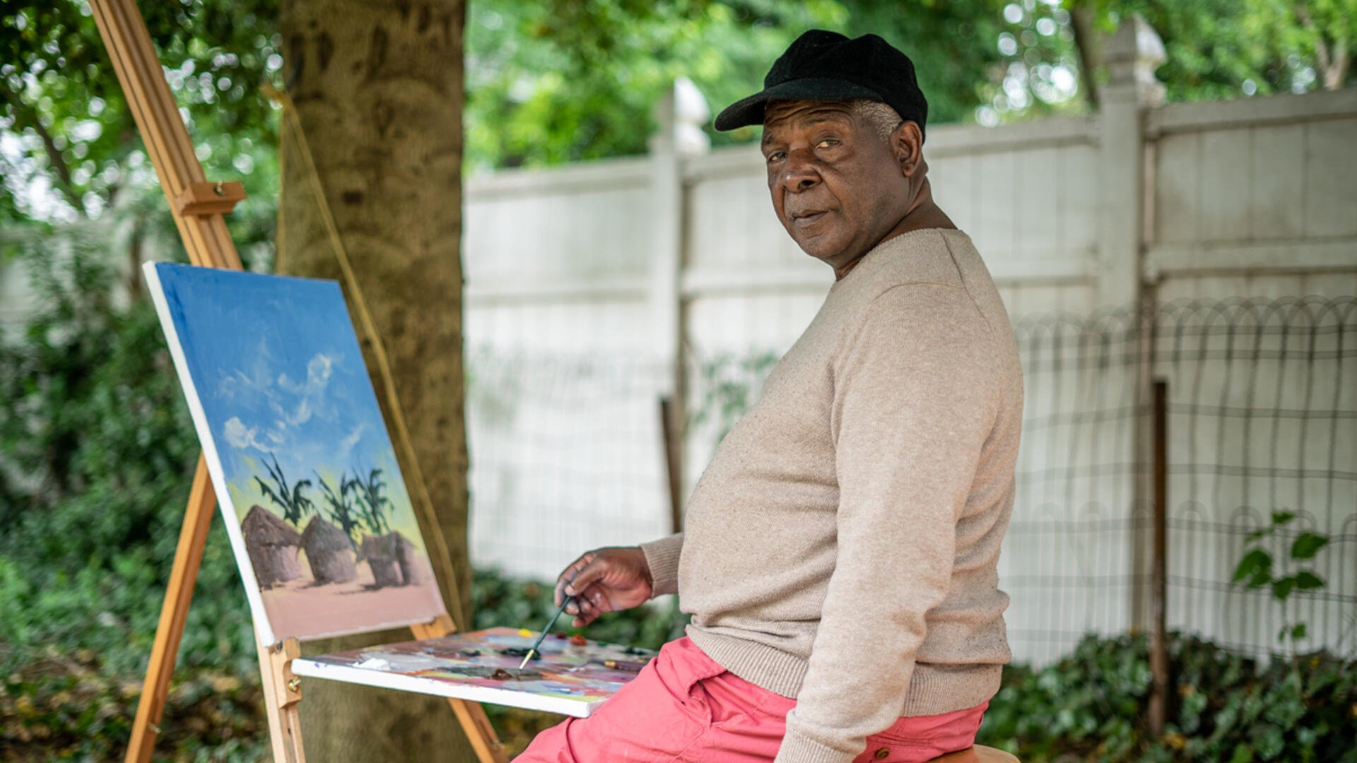 Congolese artist Muyambo Marcel Chishimba site outside at his easel painting a landscape 