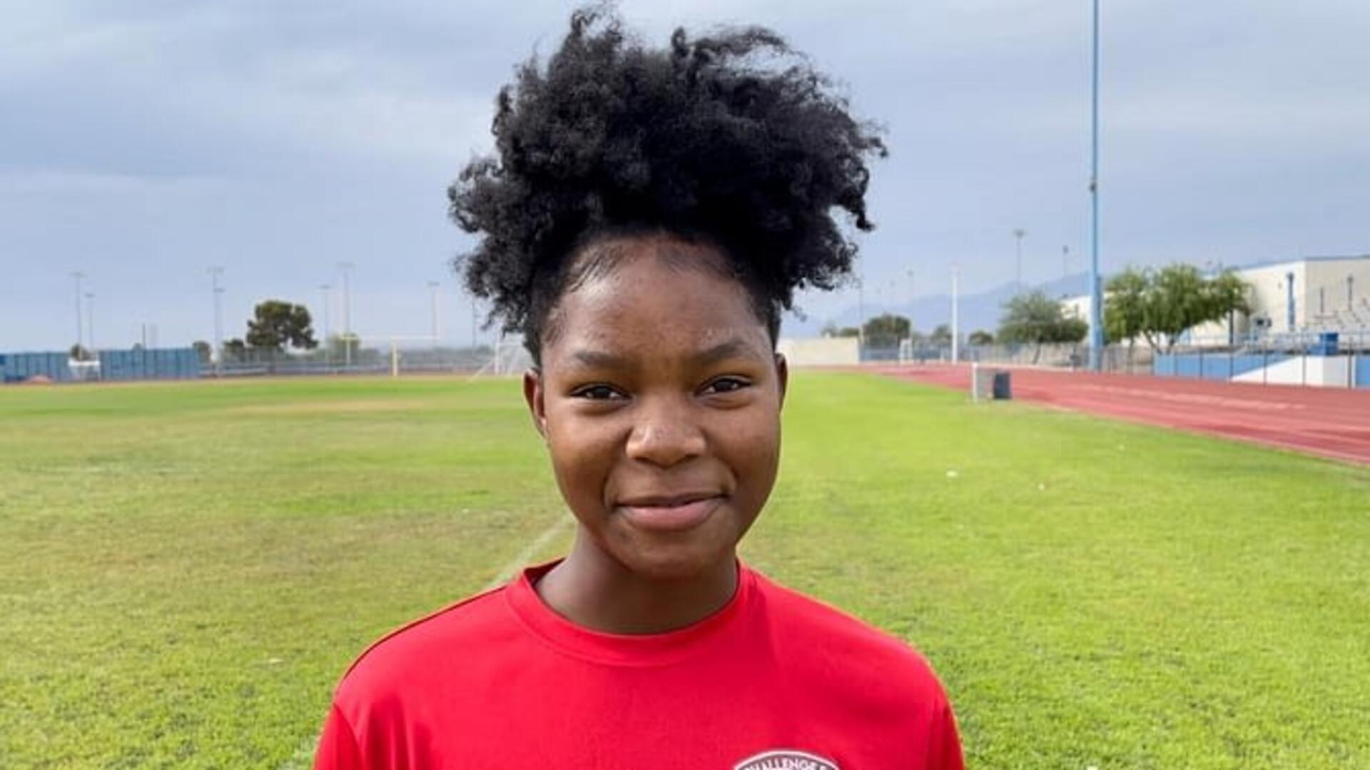 Kezia playing soccer Wearing a red shirt and smiling, Kezia looks at the camera while on a soccer field