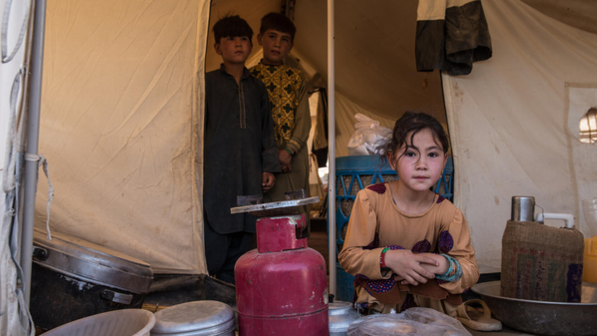 Three children at the entrance to a tent in Badghis, Afghanistan where their family is living after being displaced by drought.