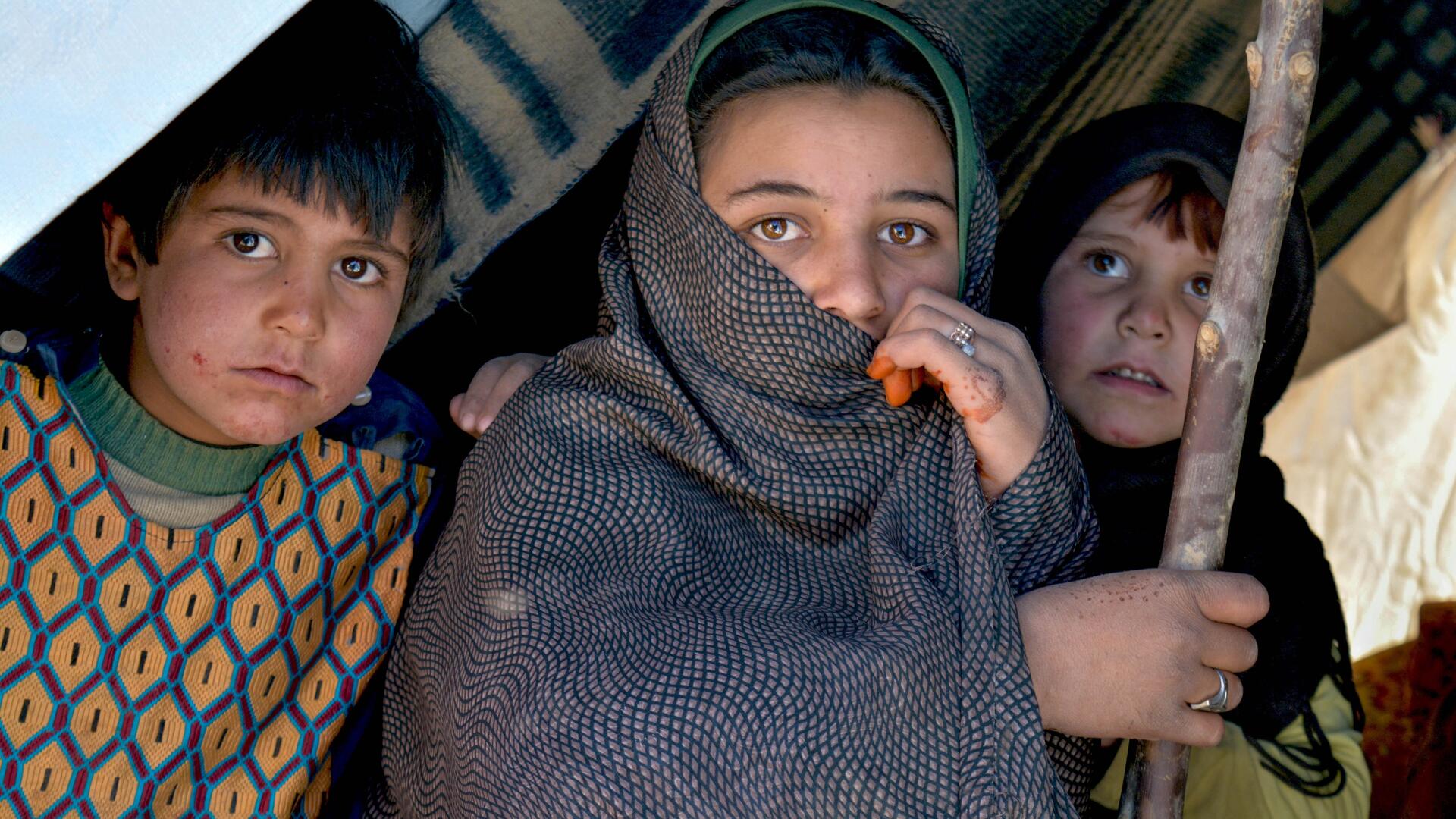 Three Afghan children sit inside a makeshift tent