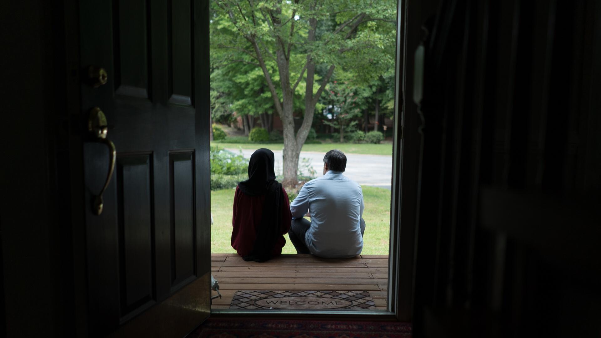 Afghan refugees Fatima, 19, and her father Abdul, 52, sit on the wooden front steps of a Virginia house looking out at the trees in the yard  
