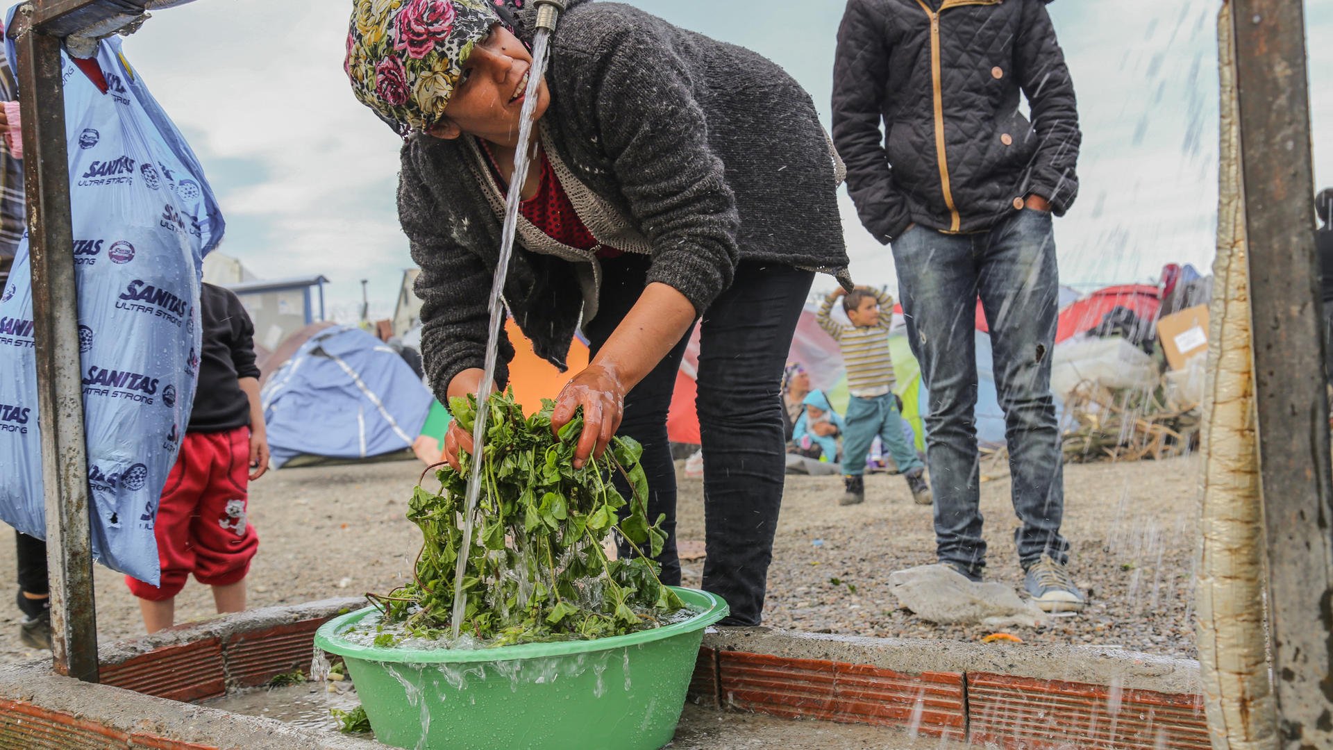 A woman washes vegatables at an IRC-installed water tap in Idomeni, Greece