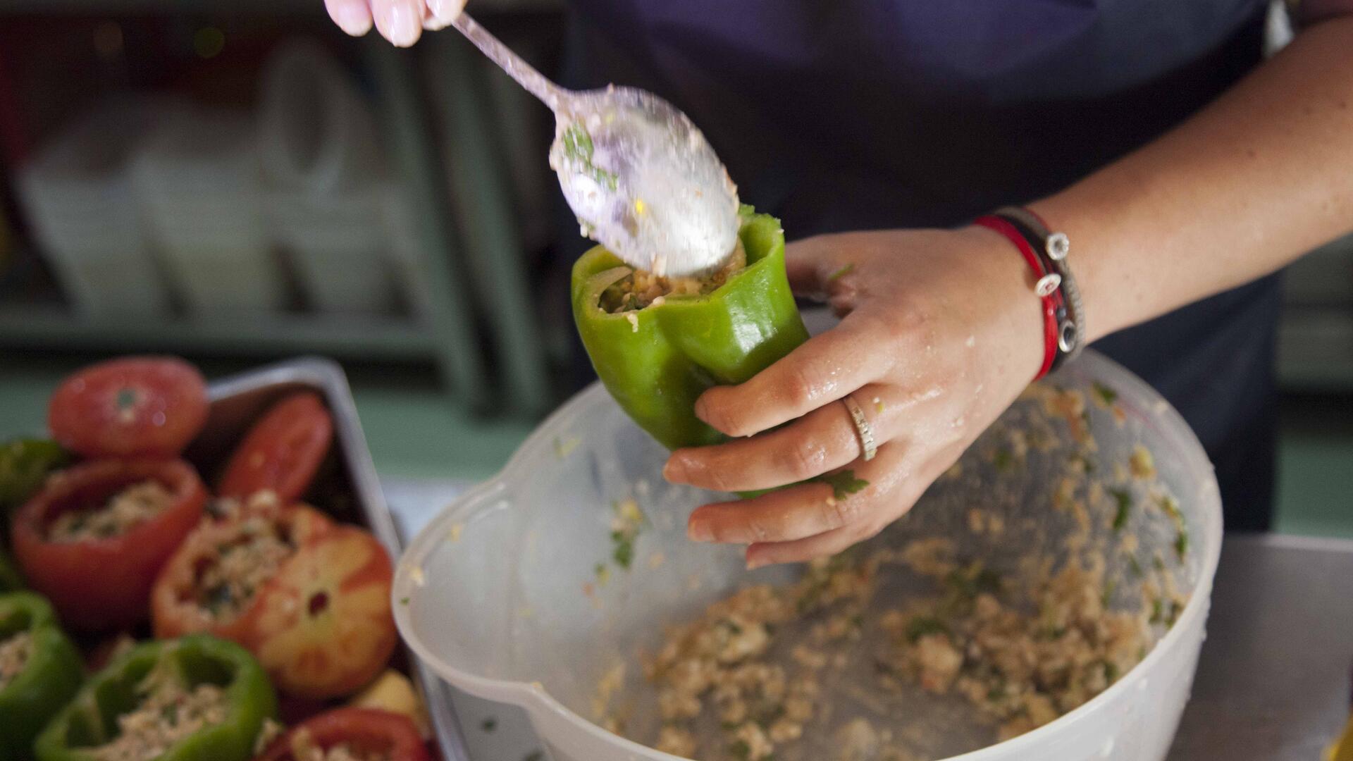 Dimitra prepares her stuffed peppers. A woman stuffs a pepper with filling.