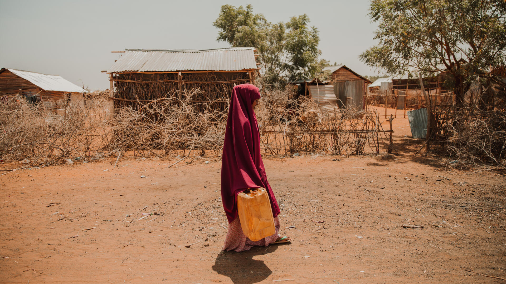 In Ethiopia, a girl walks along a dusty village lane carrying a jerry can to collect water for her family.