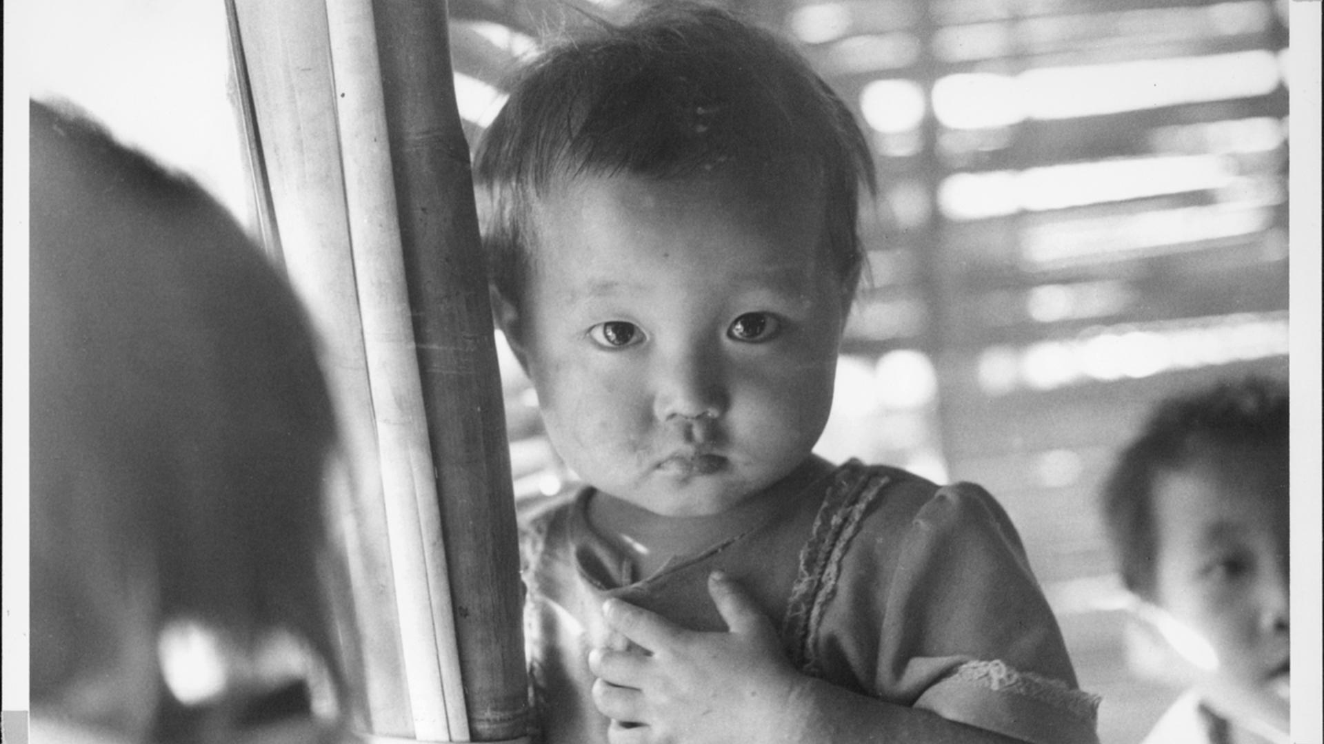 A young girl from Southeast Asia looks at the camera with a serious expression.
