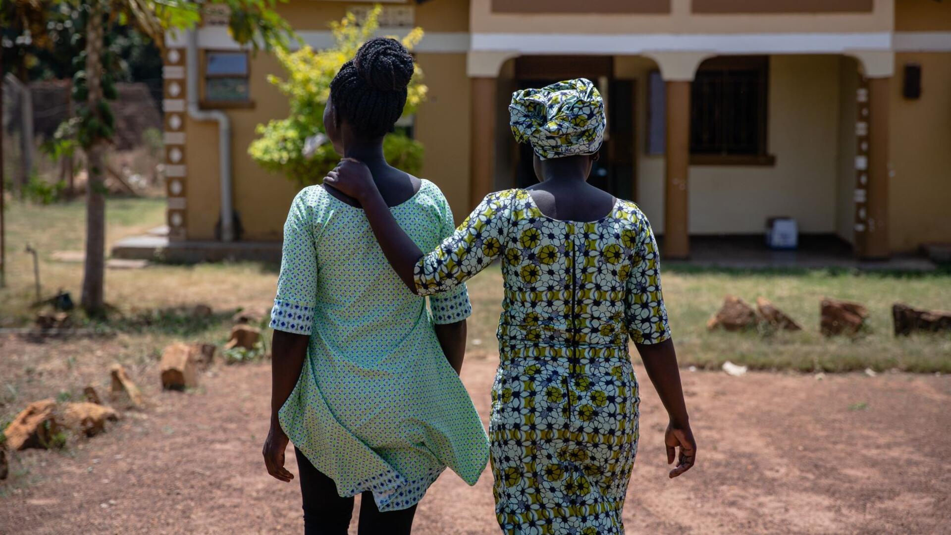 Grace and her colleague Fatuma Jamila walk outside with their back to the camera. Fatuma has her hand on Graces back.