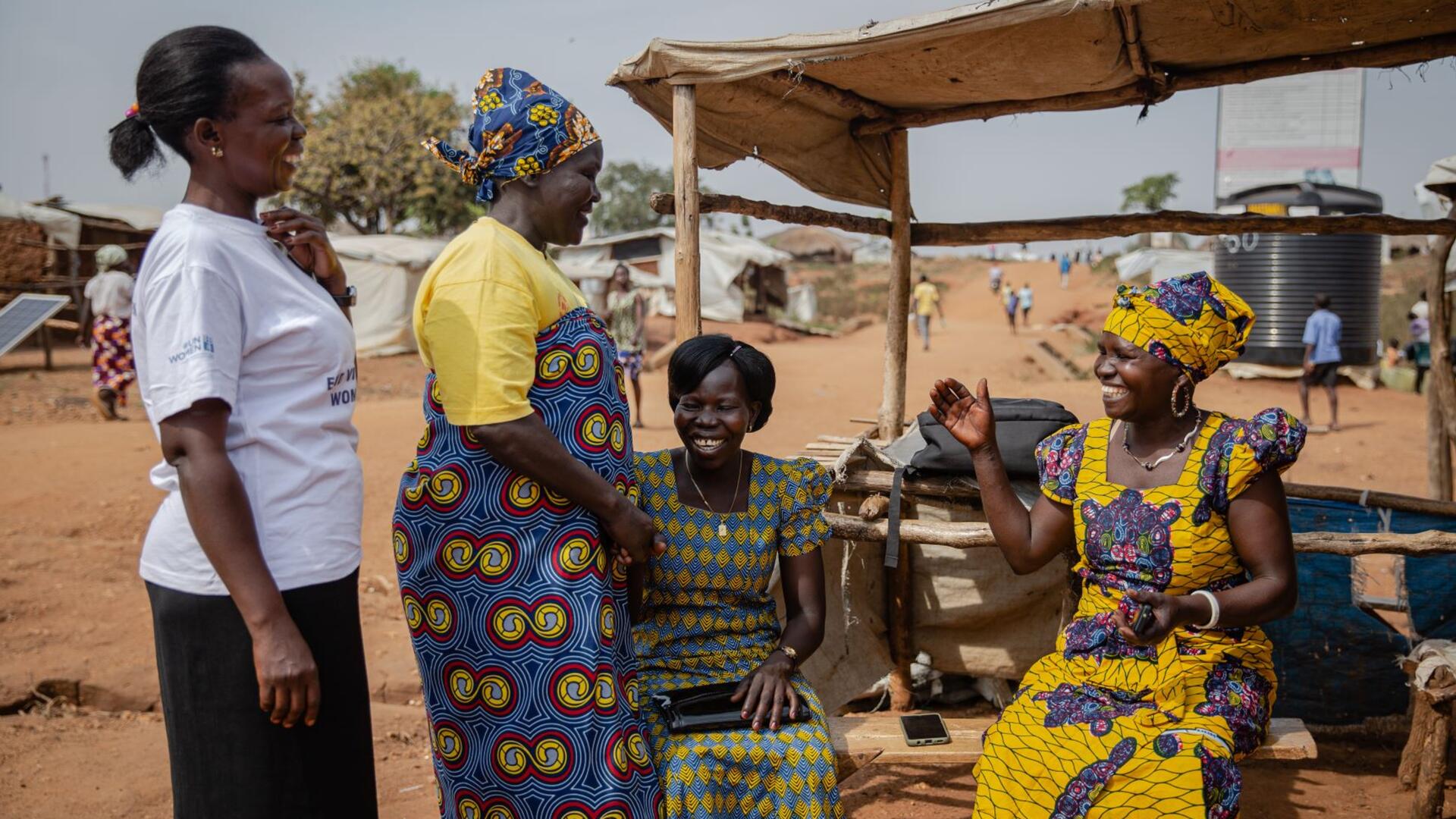 Foni Grace with other women in Togoleta. They are outside, two are sitting and two are standing, and they are laughing. 