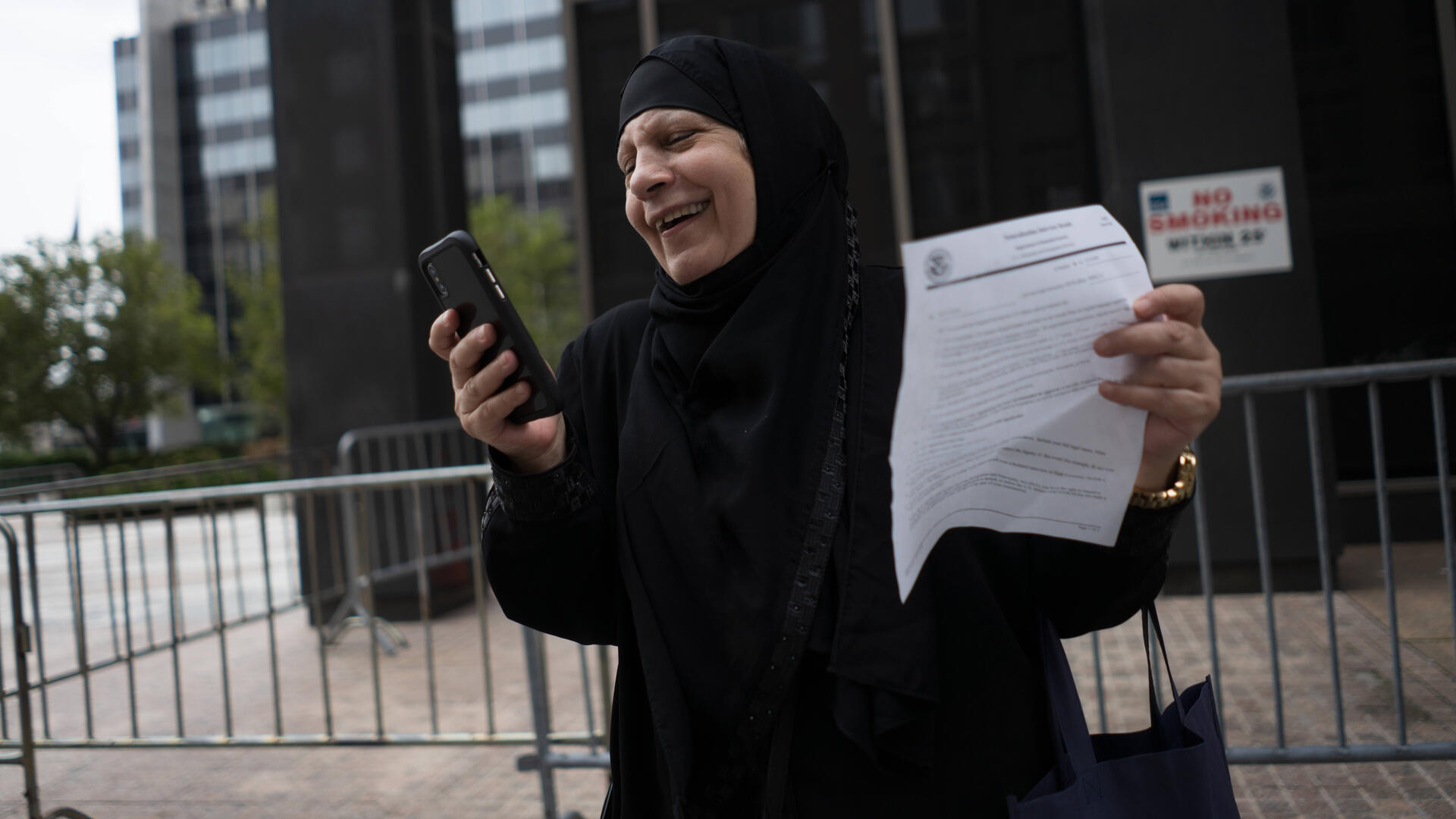 Maha calling her son in Dubai Maha smiles and holds her cell phone in one hand and an official-looking piece of paper in a another. She is standing outside the Jacob K. Javits Federal Building in lower Manhattan.