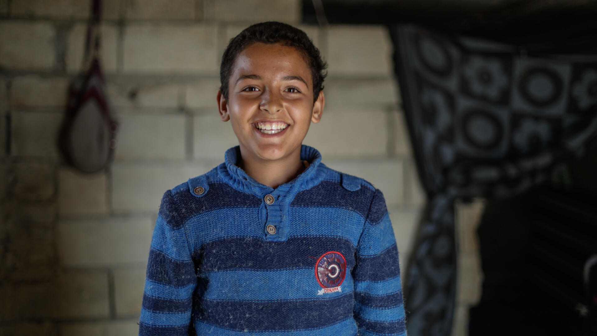 Tareq in his home Tareq, wearing a blue and white sweater, smiles for the camera in his home.