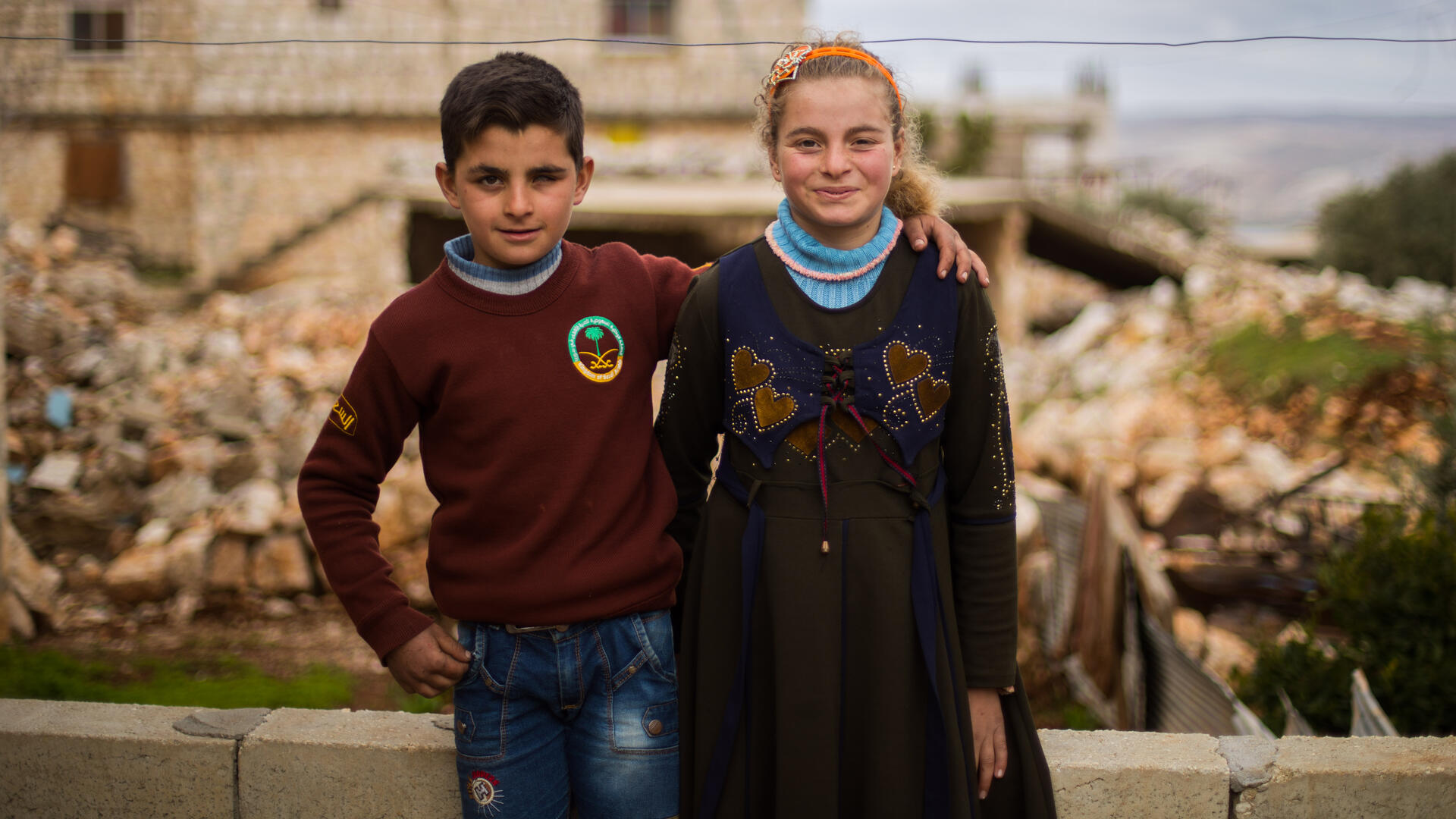 Aisha and Ali outside their home Aisha and Ali smile and pose outside their home. Ali has her arm around his sister.