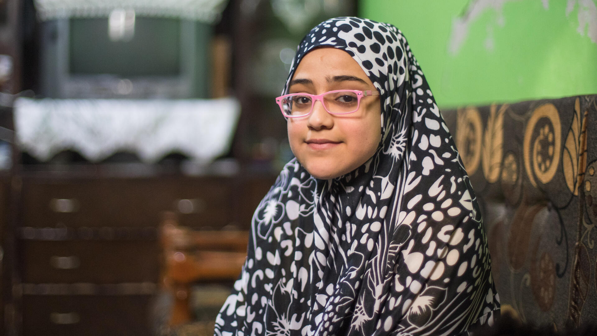 Salam sits on the ground and poses for the camera in her home