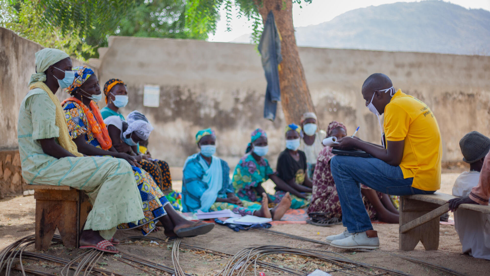Along with other parents in her community in Cameroon, Zara attends sessions at the IRC Safe Spaces targeted towards caregivers. 54-year-old Zara Tapita sits on a wooden bench with other parents listening to an IRC staff member leading a session for caregivers, to help them ensure their children can learn and thrive despite crises.