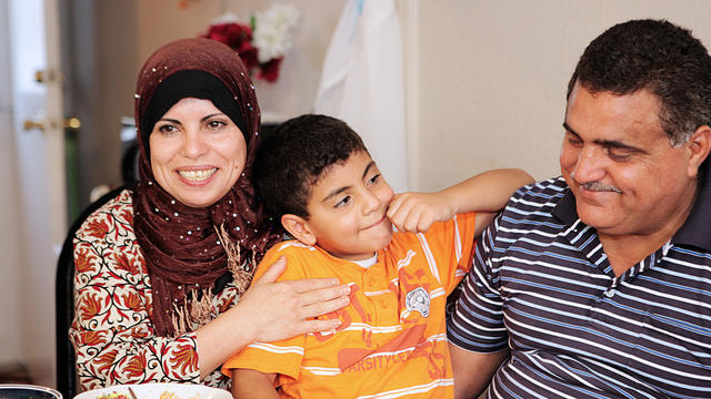 Man, woman, and child all smile together as they look at one another.