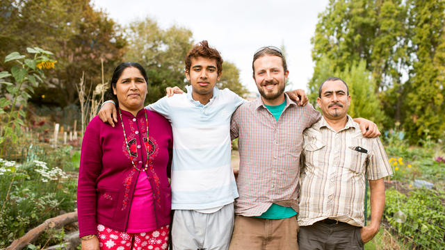 Kapil, Chandra and Chhali Manali, with garden coordinator Zack Reidman, tend the gardens at Laney College as part of Oakland's New Roots program. Four people pose for a picture outdoors in a garden.