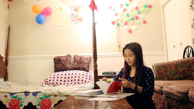Teenage girl sits in her bedroom while doing schoolwork.