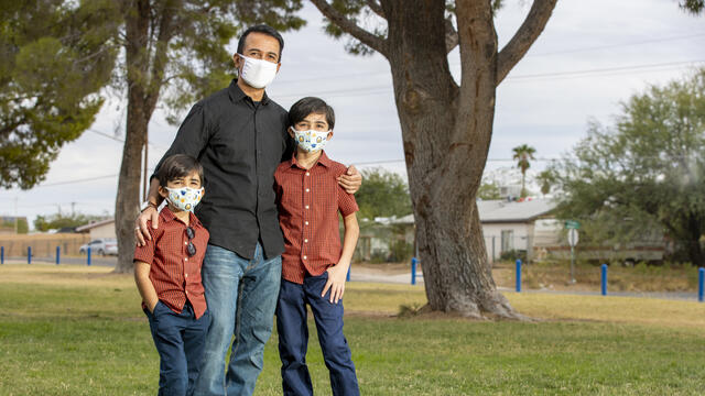 A man stands with his arms around his two young sons in Pima County, Arizona. They are wearing facemasks to protect them from COVID-19.