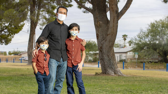Together with the Pima County Health Department, the IRC is providing COVID-19 testing, health education and community outreach to refugee, immigrant, and other families. Photo: Pima County Communications Office A man stands with his arms around his two young sons in Pima County, Arizona. They are wearing facemasks to protect them from COVID-19.